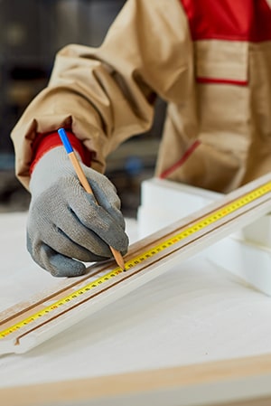 Trabajador midiendo madera para muebles personalizados.